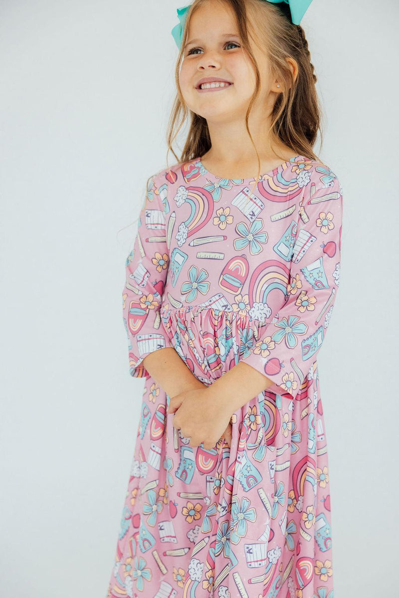 Close-up of a smiling girl in the Dream Big Little One 3/4 Pocket Twirl Dress, displaying the fun colors and prints of the dress.