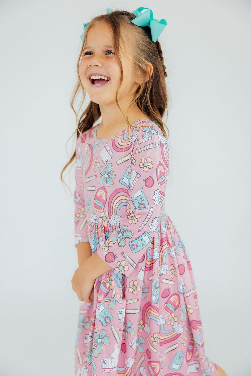 A happy child in the Dream Big Little One 3/4 Pocket Twirl Dress by Mila & Rose®, featuring a fun print, joyfully posing against a clean background.