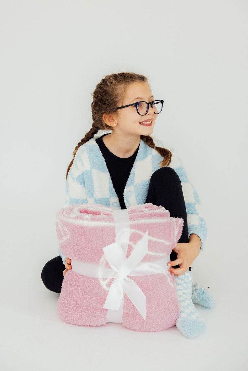 A cheerful girl smiling while holding a neatly tied bundle of the Light Pink Cowgirl Cozy Blanket, perfect for cozy moments.