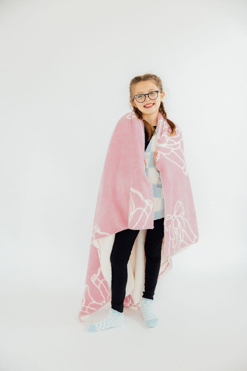 A girl wearing glasses joyfully wrapped in the Light Pink Cowgirl Cozy Blanket, showcasing its softness and warmth.