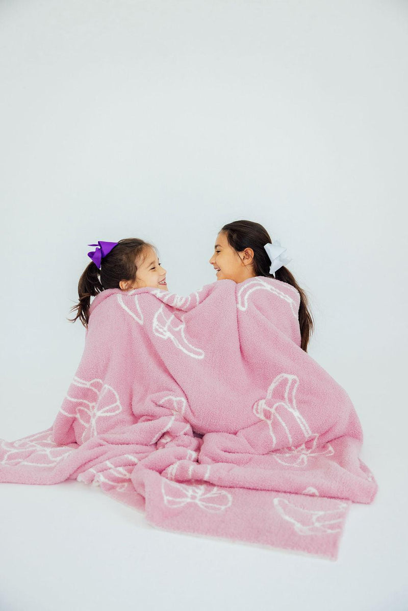 Two sisters cozied up together in the Light Pink Cowgirl Cozy Blanket, sharing smiles and warmth in a delightful moment.