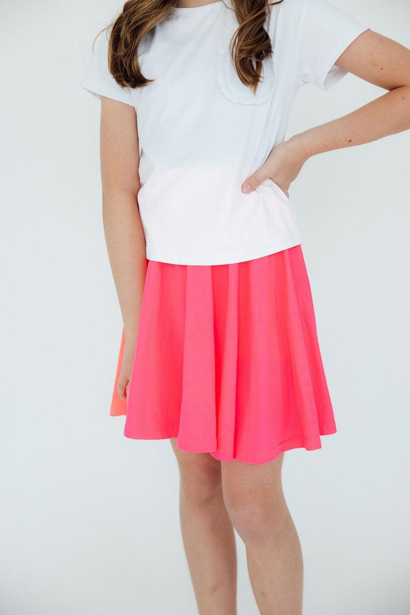 Close-up of a girl in a Neon Pink Twirl Skort from Mila & Rose, emphasizing the vibrant pink fabric and the stylish design as she poses with her hand on her hip.