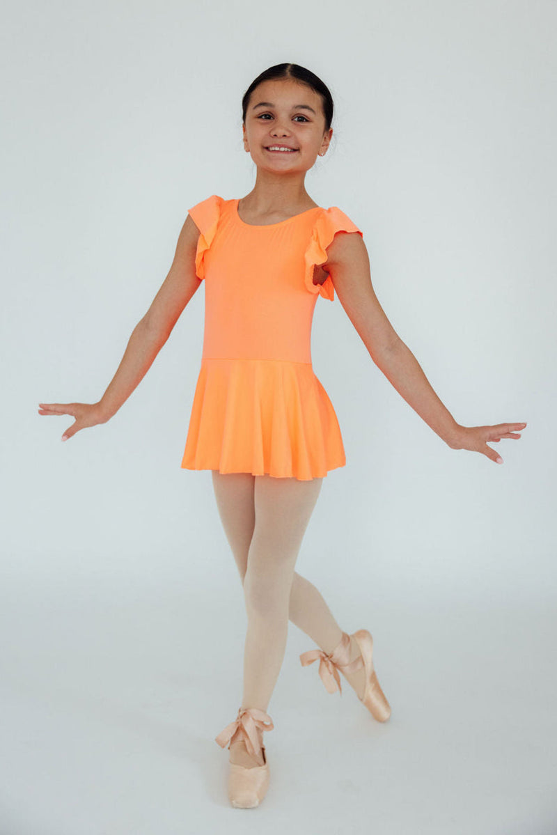 Child model wearing the Neon Coral Short Sleeve Twirl Leotard, twirling gracefully in a dance pose with ballet shoes.