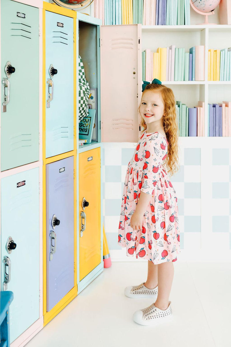 Girl standing by colorful lockers in the Star Student 3/4 Sleeve Pocket Twirl Dress by Mila & Rose®, showcasing a stylish look perfect for school.