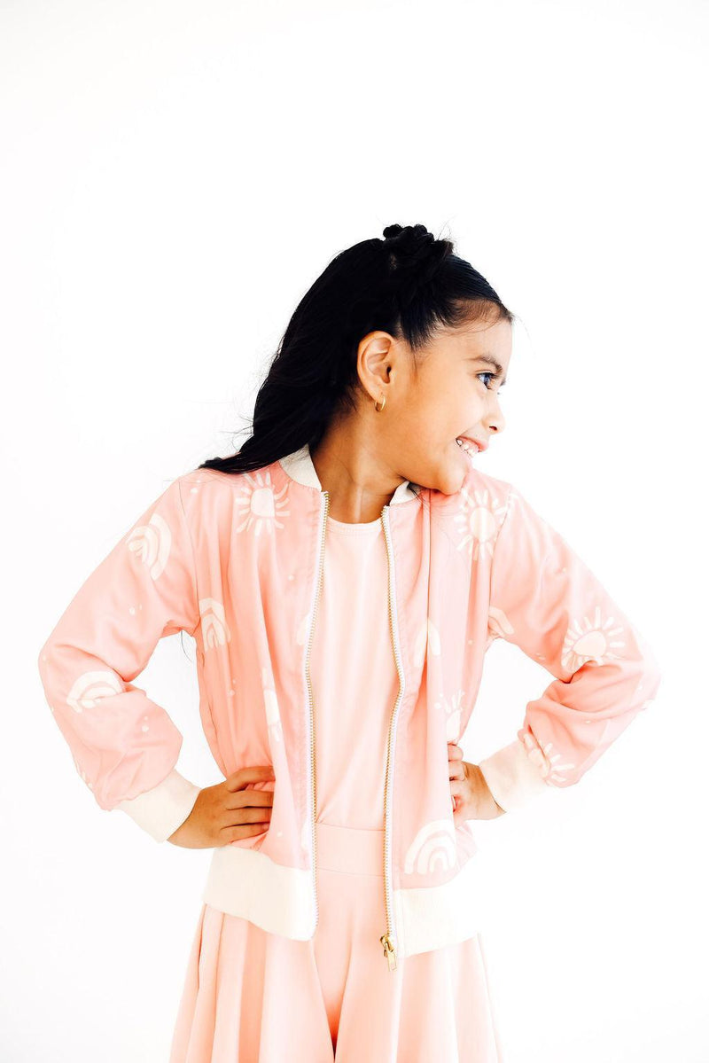 A playful girl in the Soft Pink Sun Satin Jacket by Mila & Rose, showcasing a fun side pose with her hands on her hips. The soft pink fabric and joyful prints make it a perfect stylish choice.