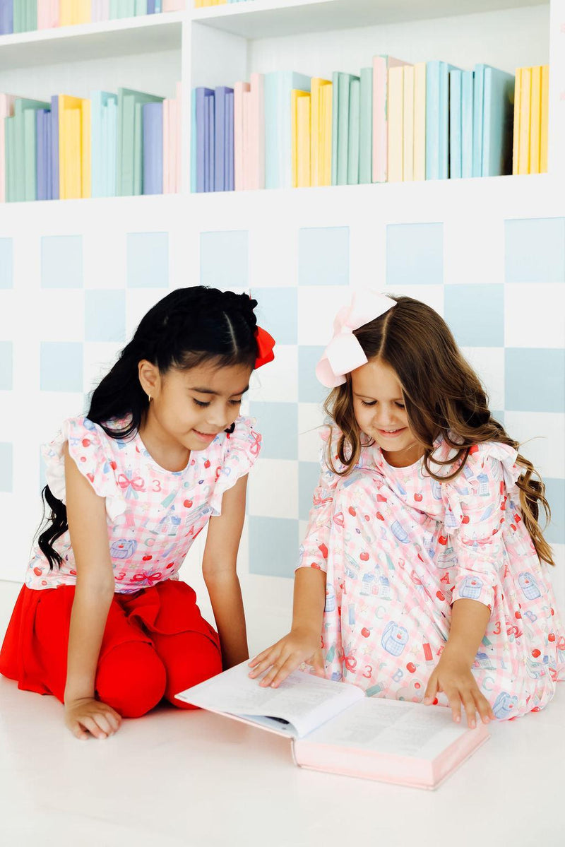 Two happy girls in 'School Days 3/4 Ruffle Twirl Dress' by Mila & Rose ®, sitting on the floor, reading a book together. Ideal for fun outings or school events.