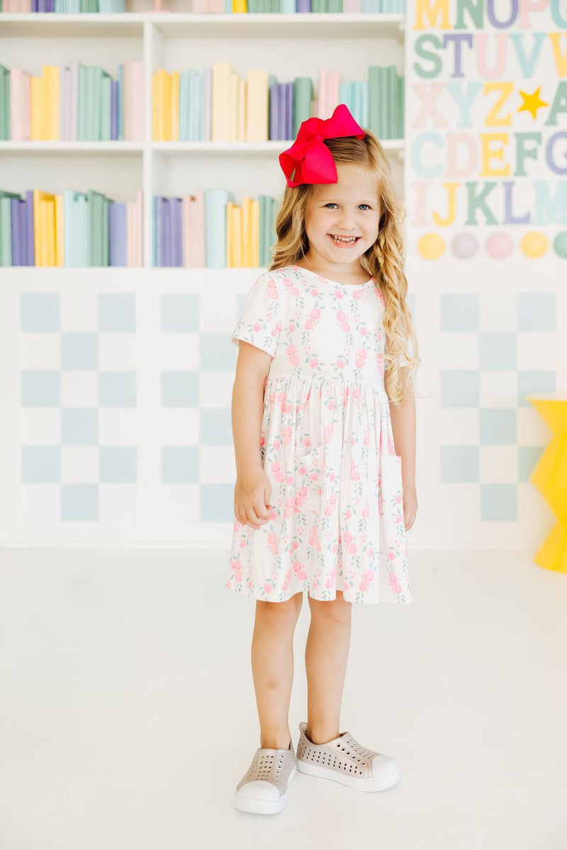 A pair of happy girls wearing matching Rosie Posie S/S Pocket Twirl Dresses by Mila & Rose, showing off their twirls and coordinated styles.