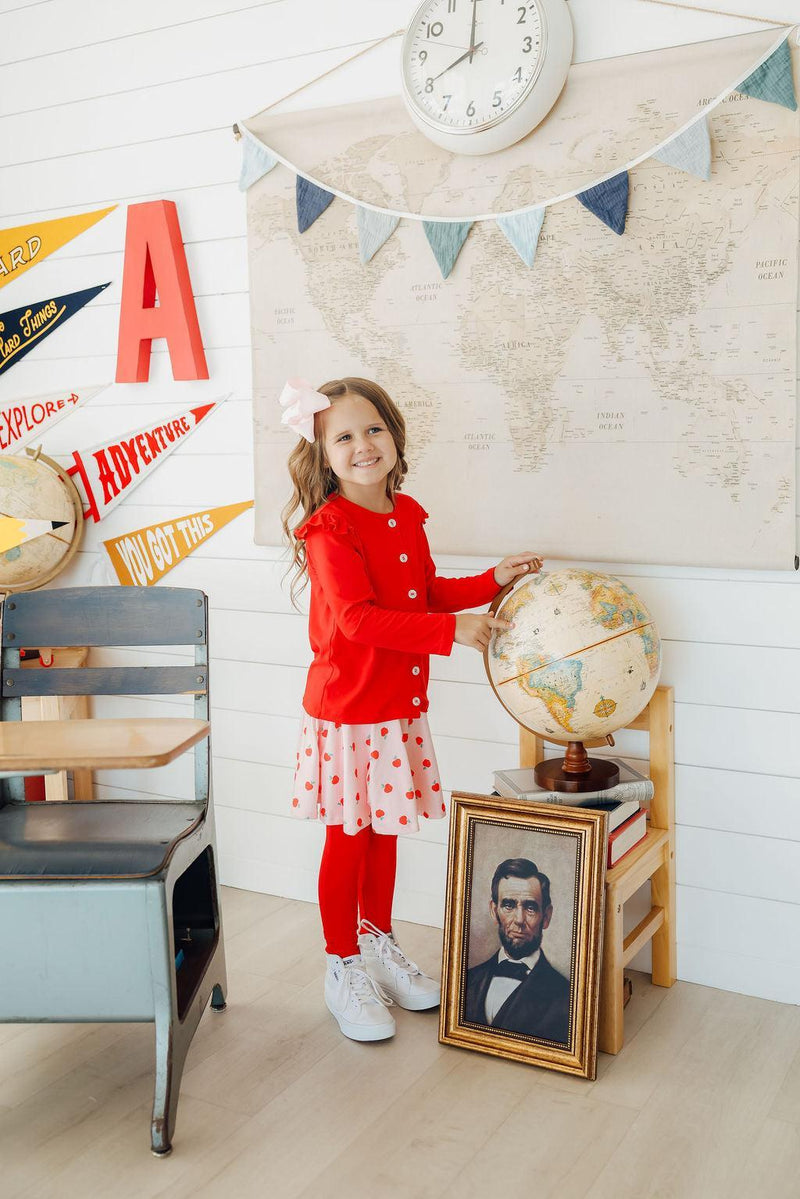 A girl exploring and touching a globe while wearing An Apple a Day Twirl Skeggings for Girls, blending fun and fashion in these playful skeggings for girls.
