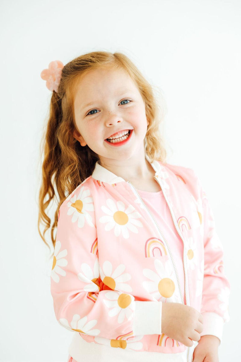 Close-up of a girl in the You are My Sunshine Satin Jacket by Mila & Rose®, showcasing the vibrant pink fabric adorned with daisies and rainbows, highlighting her joyful expression.