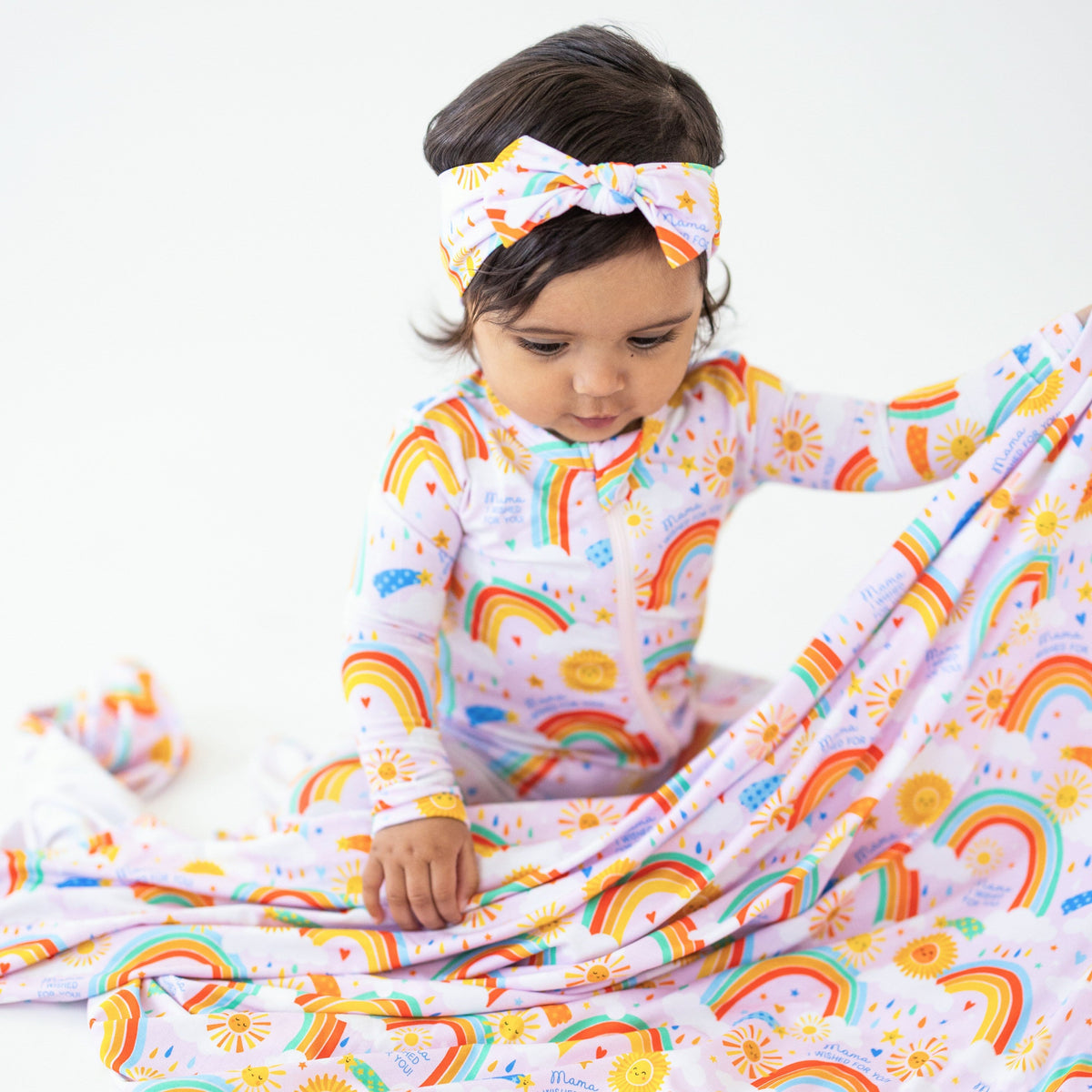 A baby playing with The Forever Swaddle Blanket | Here Comes the Sunshine (Pink), displaying vibrant rainbow and sunshine patterns.