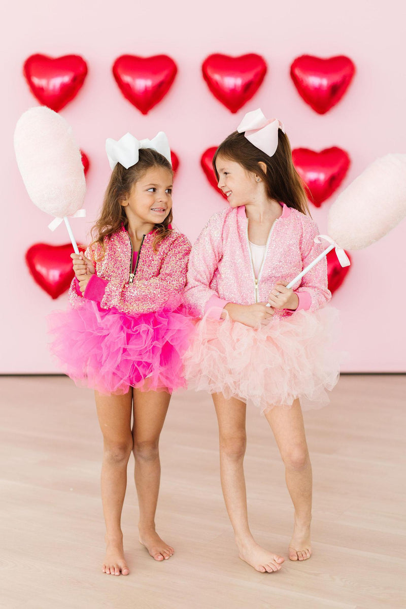 Two girls smiling in matching outfits, one wearing the 'Elana' Ballet Pink Tank Tutu Leotard, celebrating fun moments with cotton candy.