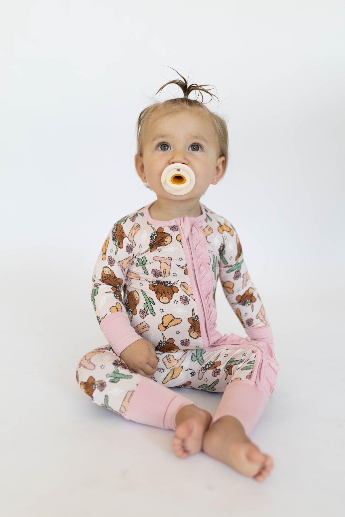 Baby in pink highland cow romper looking up against white background