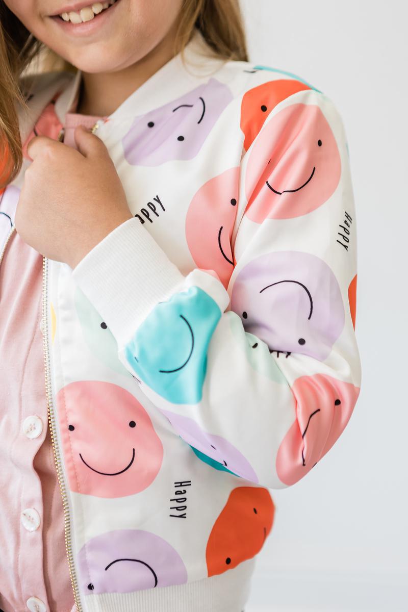 Close-up of a girl in the 'Happy Days' Satin Jacket for Girls, highlighting the vibrant smiley face design, perfect for adding fun and flair to her outfit.