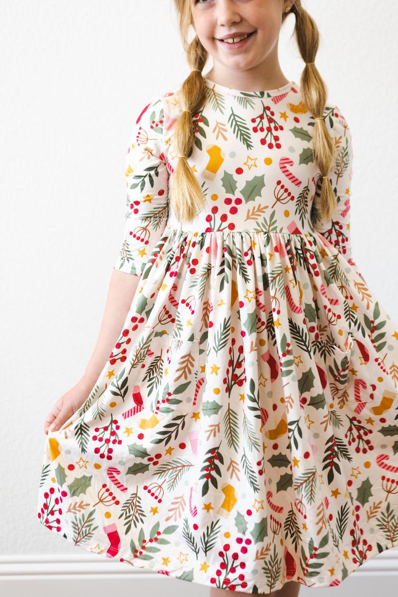 A young girl happily posing in the 'Holly Jolly Christmas' 3/4 Sleeve Pocket Christmas Twirl Dress for Girls, highlighting the playful design.