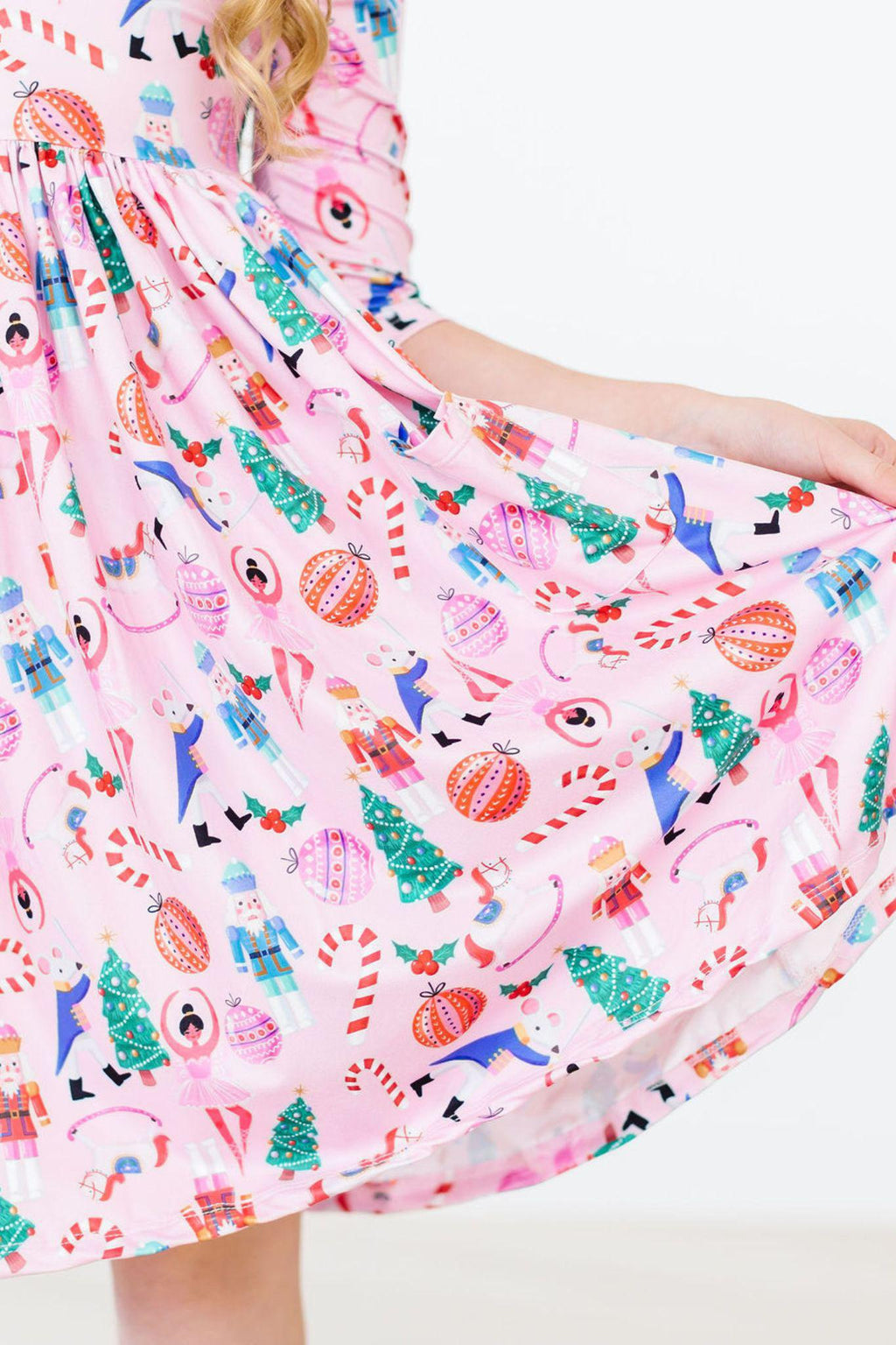 Close-up of the Sugarplum Fairy 3/4 Sleeve Pocket Twirl Dress featuring a playful pink fabric with festive prints including Christmas trees, candy canes, and whimsical animals.