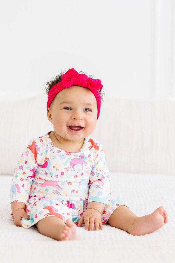 Baby girl wearing Mila and Rose sleeve bodysuit for babies with colorful unicorn print and pink headband