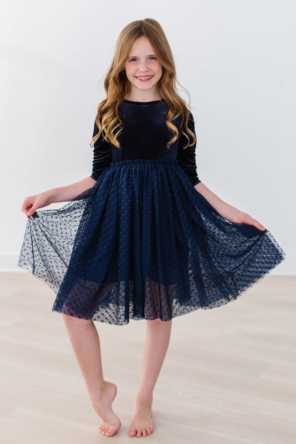 A joyful girl modeling the Light Navy Velvet Tutu Dress, twirling with a smile, showcasing the luxurious velvet and playful tulle skirt in a bright, airy setting.
