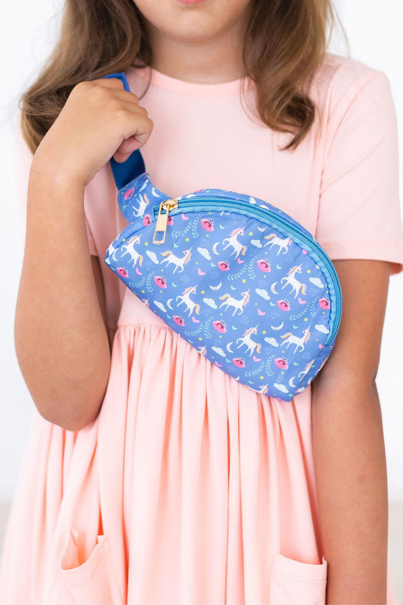 A young girl in a pink dress holding the Blue Moon Belt Bag, emphasizing its unique unicorn print and hands-free design perfect for resourceful young adventurers.