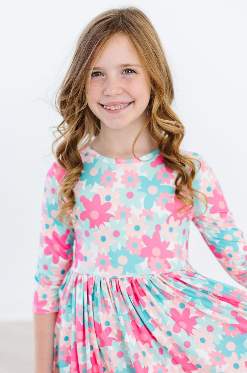 A cheerful girl wearing the Petal Perfection 3/4 Sleeve Pocket Twirl Dress, featuring a vibrant floral pattern in pink and blue, showcasing her joyful smile and playful spirit.
