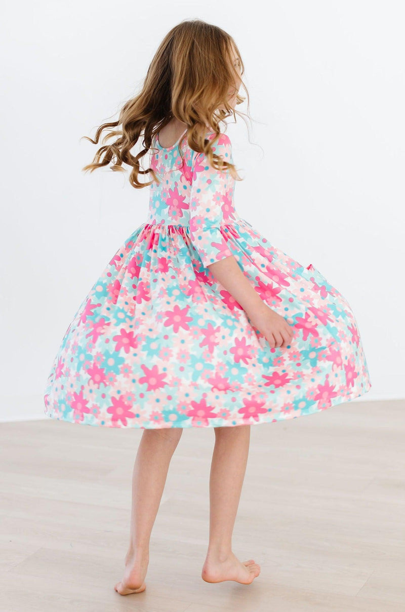 The back view of a young girl spinning joyfully in the Petal Perfection 3/4 Sleeve Pocket Twirl Dress, showcasing the vibrant colors and its twirl-friendly shape for carefree adventures.