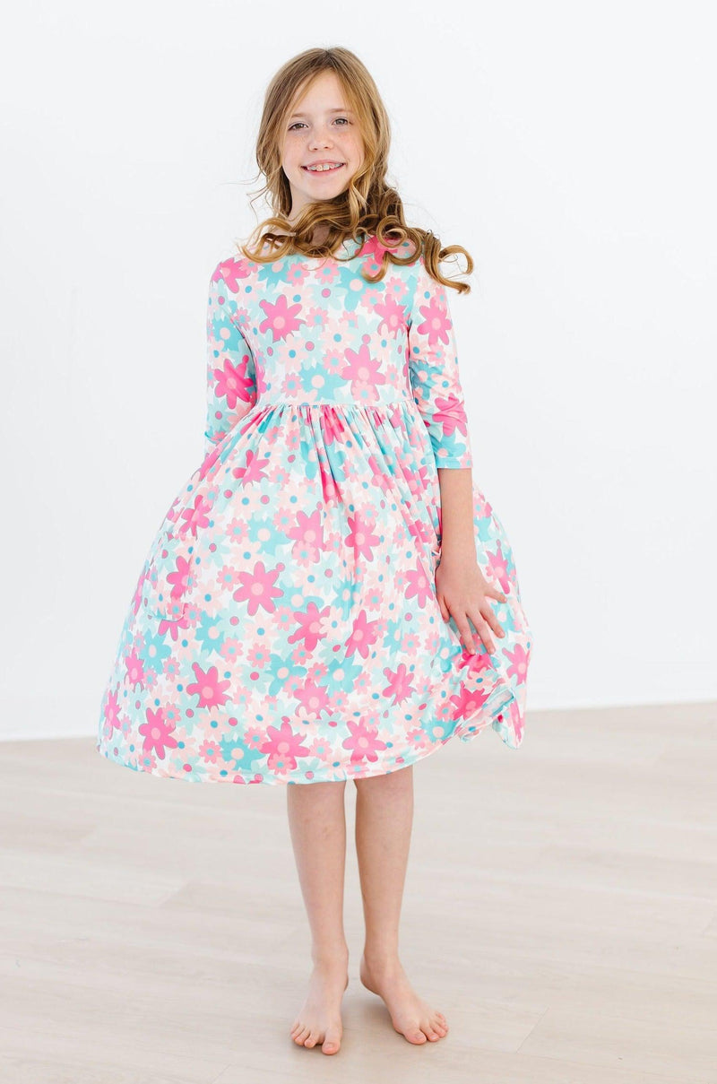 A joyful girl standing confidently in the Petal Perfection 3/4 Sleeve Pocket Twirl Dress, showcasing its delightful floral design that's perfect for any occasion.
