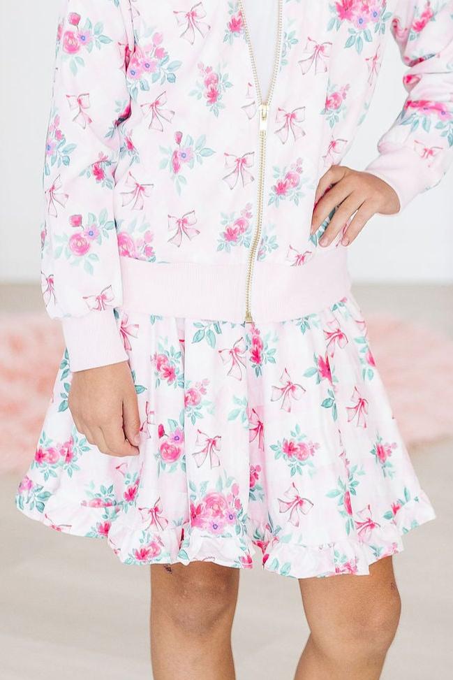 Delightful Gingham Bows Ruffle Twirl Skort showcased by a joyful child in a floral bomber jacket, perfect for spinning and twirling while looking cute.