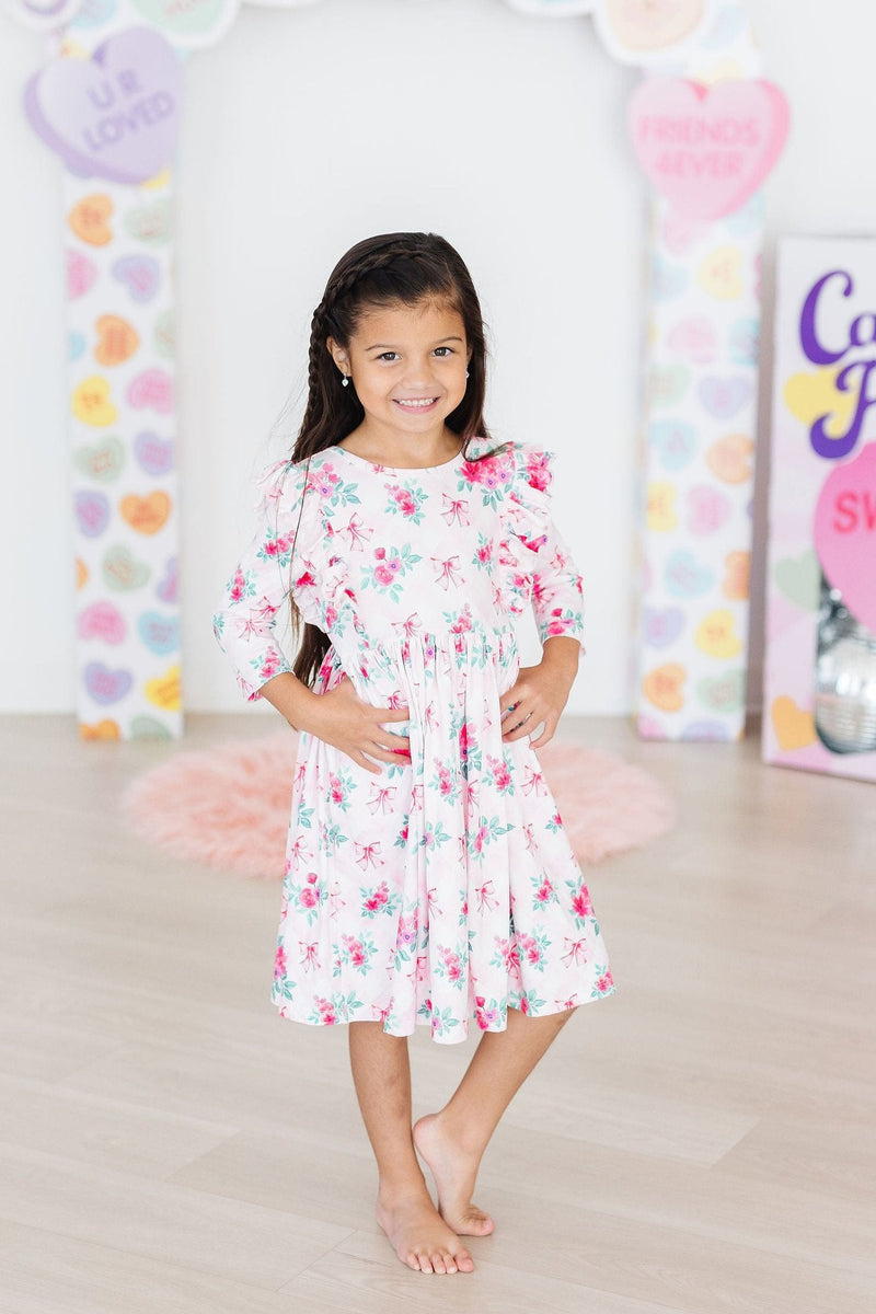 Charming little girl in the Gingham Bows 3/4 Sleeve Ruffle Twirl Dress, striking a confident pose with hands on her hips, radiating fun and style against a colorful backdrop.