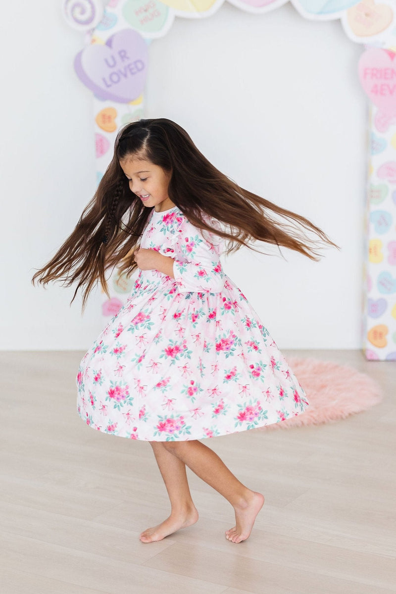 A happy little girl spinning in the Gingham Bows 3/4 Sleeve Ruffle Twirl Dress, her hair flowing around her, embodying the carefree spirit of childhood in a bright and cheerful setting.
