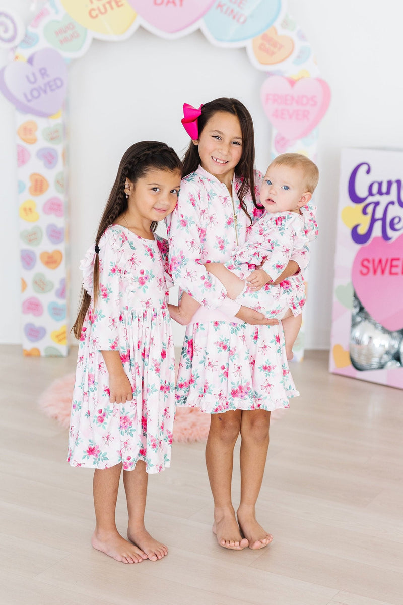 Three adorable girls, including one in the Gingham Bows 3/4 Sleeve Ruffle Twirl Dress, sharing a joyful moment together, showcasing the delightful twirl potential of their matching outfits.