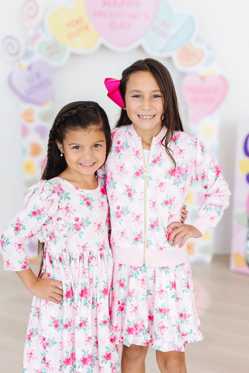 Two charming girls wearing the Gingham Bows Ruffle Twirl Skort and coordinating outfits, radiating joy and style, perfect for playful adventures.