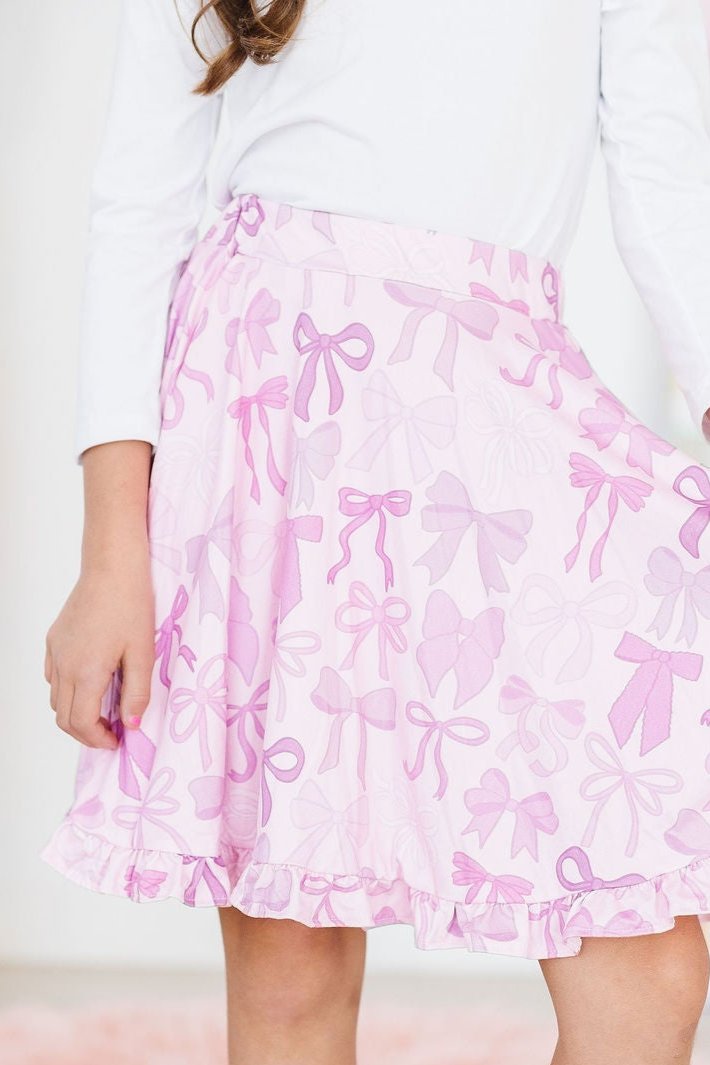 Twinkle Ties Ruffle Twirl Skort in pink with bow patterns, worn by a smiling girl, showcasing playful design perfect for active adventures.
