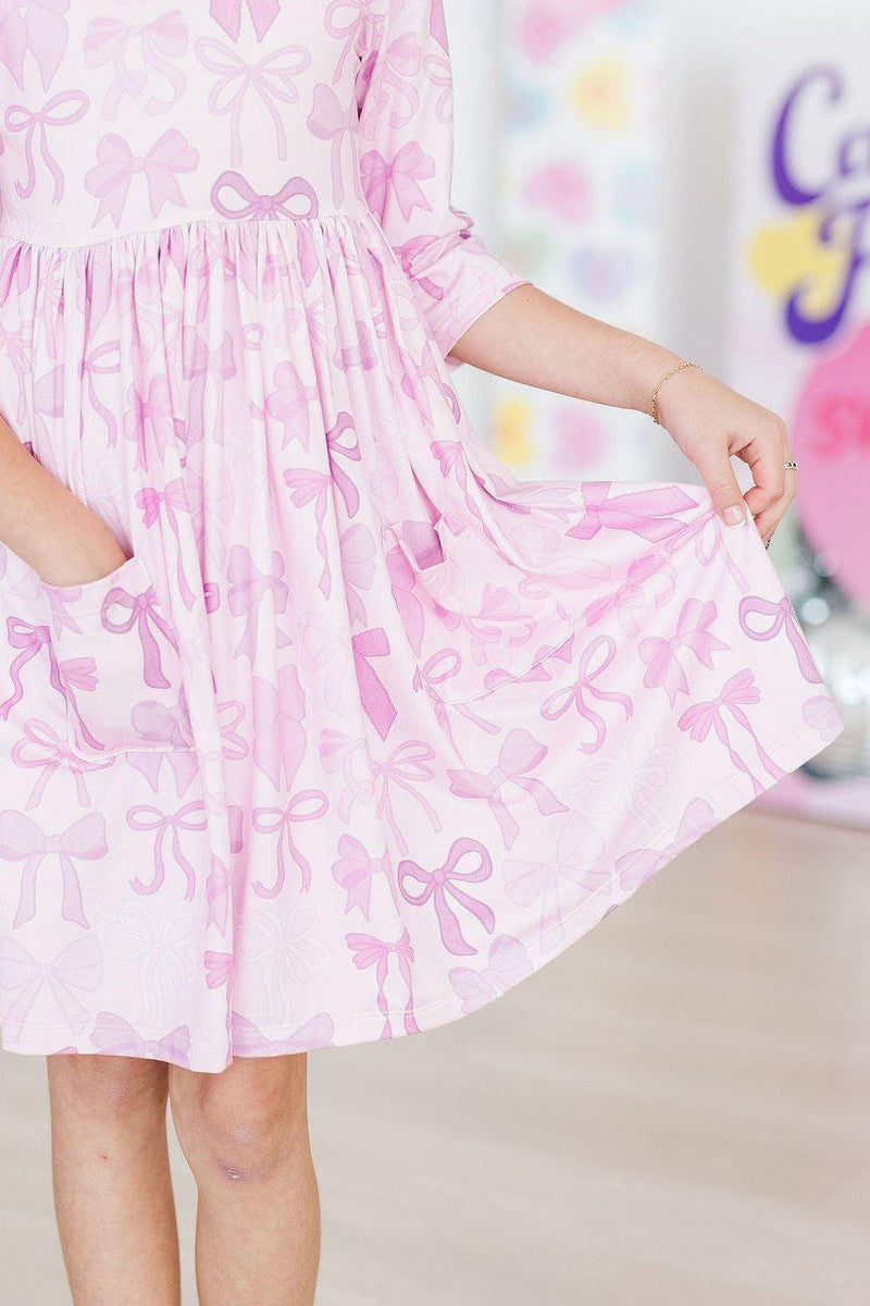 Close-up of the Twinkle Ties 3/4 Sleeve Pocket Twirl Dress from Mila & Rose, highlighting its cute bow pattern and functional pockets.