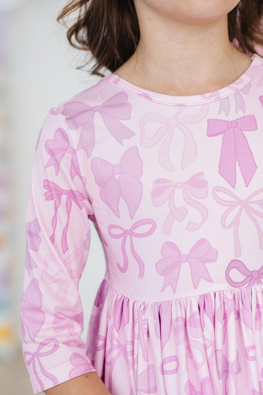 Twinkle Ties 3/4 Sleeve Pocket Twirl Dress featuring a playful pink bow print, showcasing a child in a joyful pose, perfect for twirling and everyday adventures.