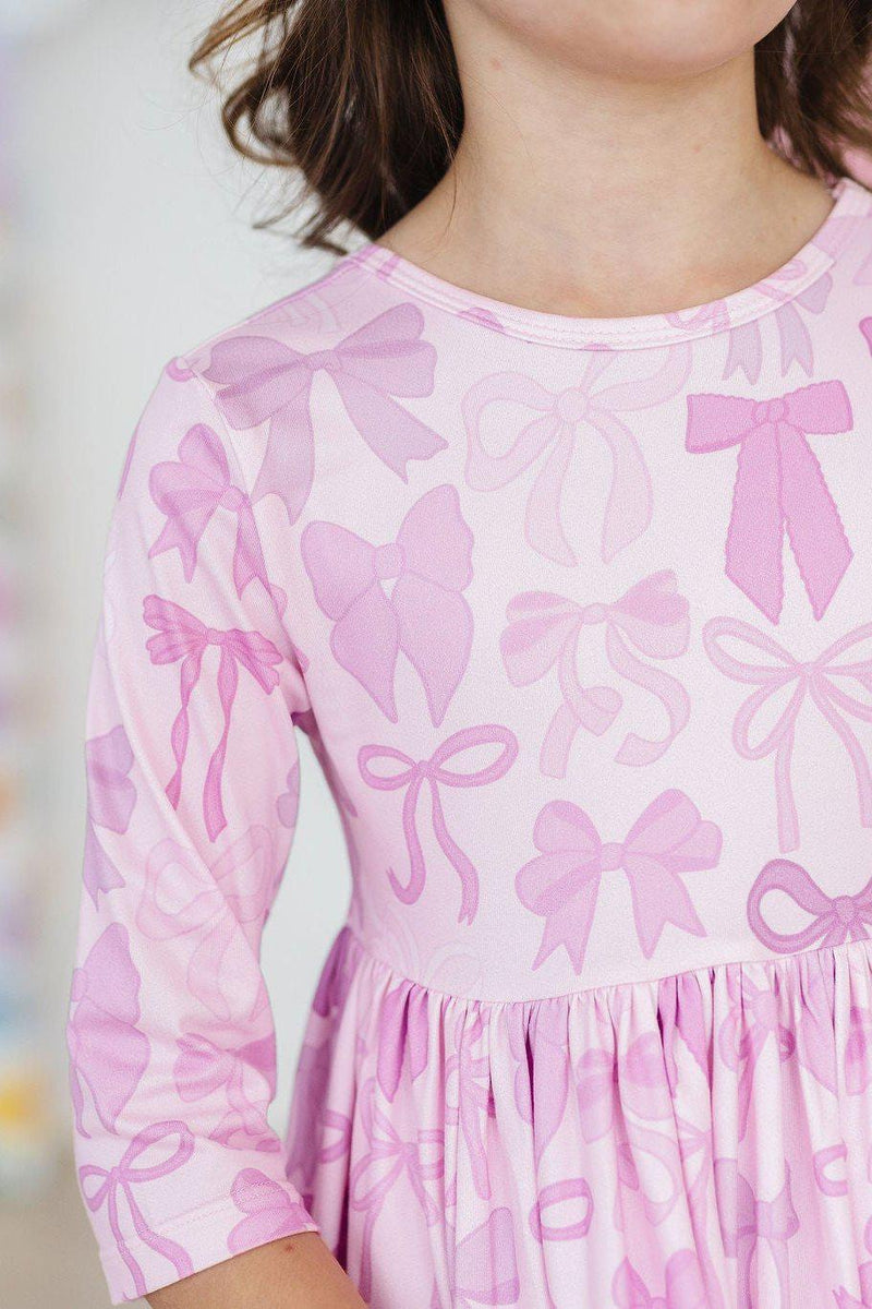 Twinkle Ties 3/4 Sleeve Pocket Twirl Dress featuring a playful pink bow print, showcasing a child in a joyful pose, perfect for twirling and everyday adventures.