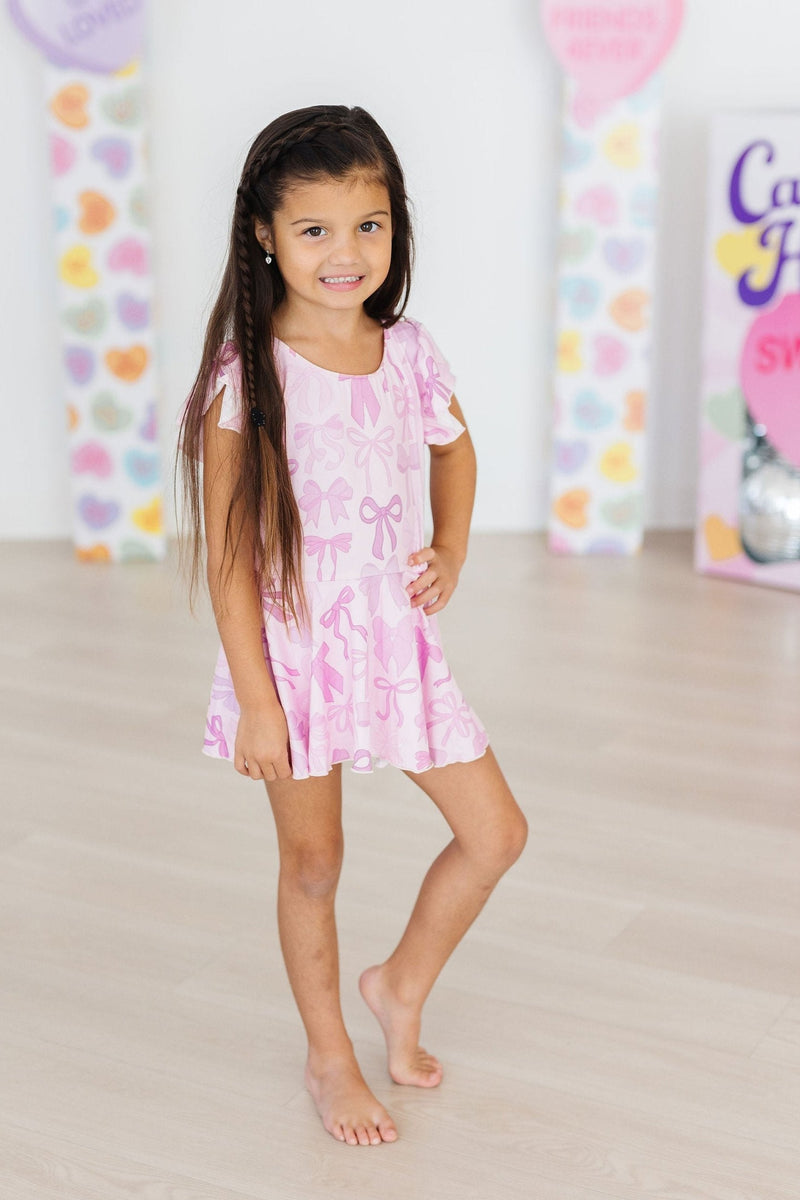 Cute young girl showcasing the Twinkle Ties S/S Twirl Leotard by Mila & Rose, featuring a playful pink design with bows, perfect for dance classes and playdates.