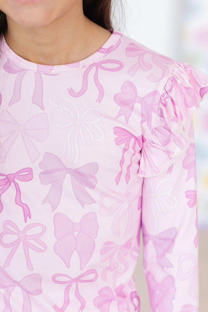 Close-up of the Twinkle Ties L/S Ruffle Tee, highlighting the delicate ruffle details and pastel pink bow print.
