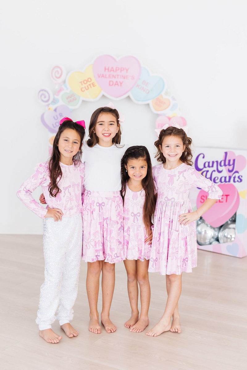 Twinkle Ties L/S Ruffle Tee worn by four girls, showcasing matching outfits with fun pink bow designs, perfect for a playful group.