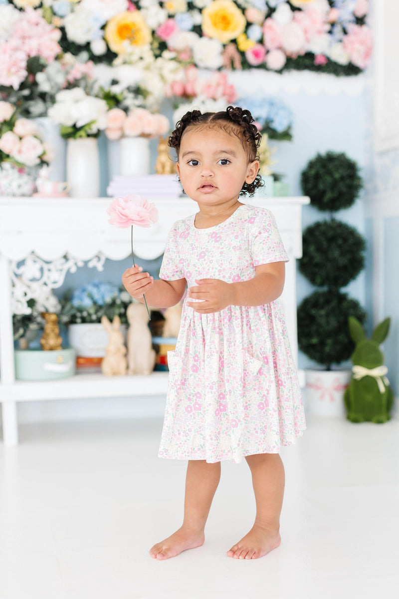 Child wearing the Blooming Beauty S/S Pocket Twirl Dress, twirling joyfully in a sunny park setting, embodying fun and grace.