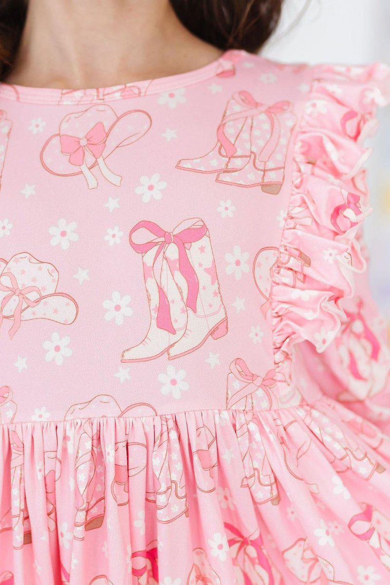 Close-up detail of the Howdy 3/4 Sleeve Ruffle Twirl Dress, featuring ruffle accents and a whimsical print of cowboy boots and bows on soft pink fabric.