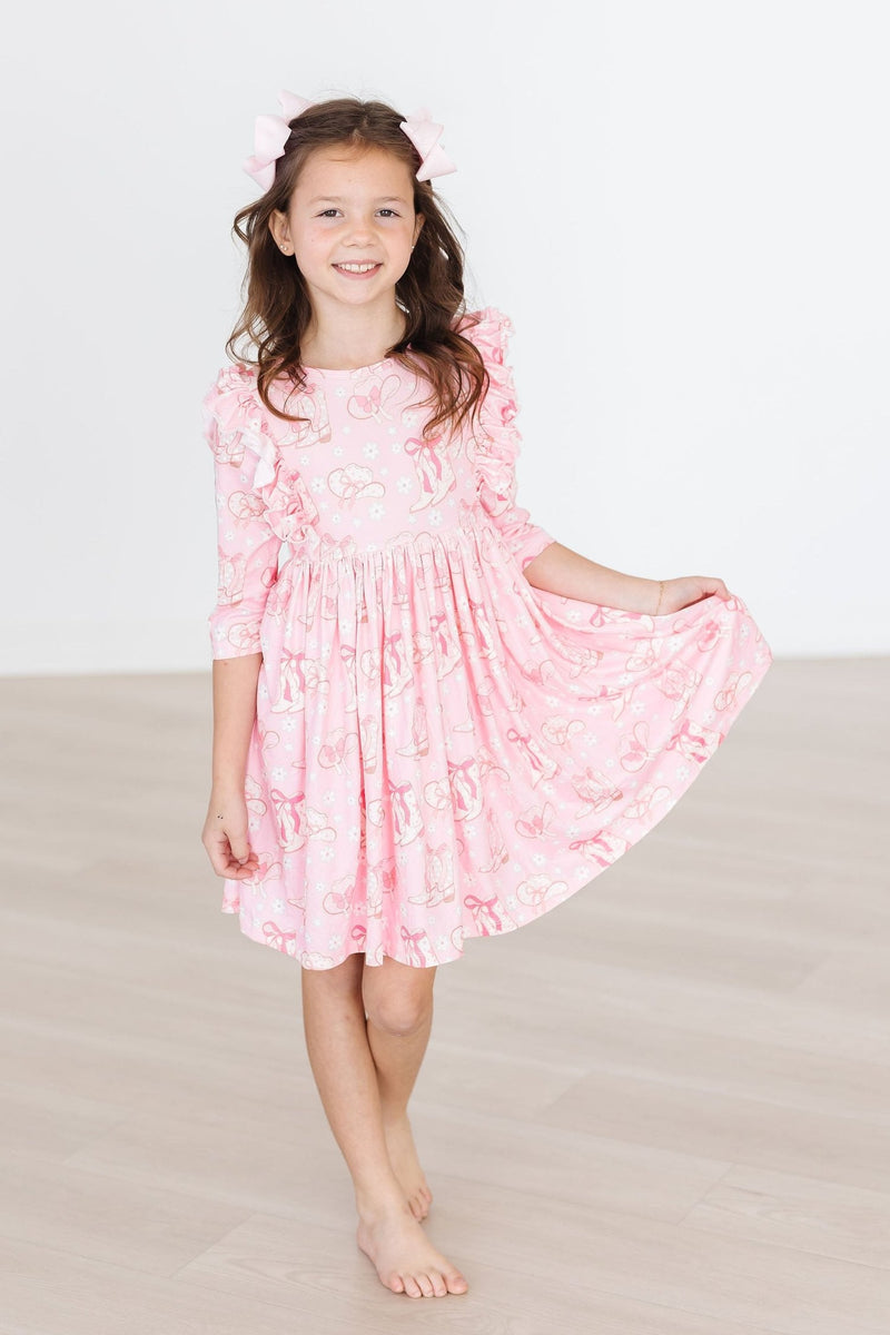 Charming girl in a Howdy 3/4 Sleeve Ruffle Twirl Dress by Mila & Rose®, gracefully smiling while showcasing its delightful pink design.