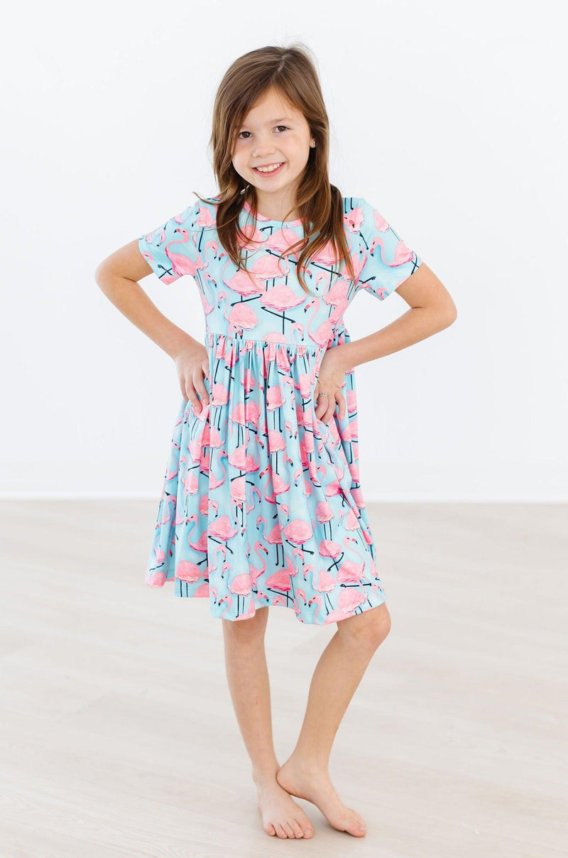 Confident young girl posing with hands on hips in the Pretty in Pink Flamingos S/S Pocket Twirl Dress, radiating playful charm.