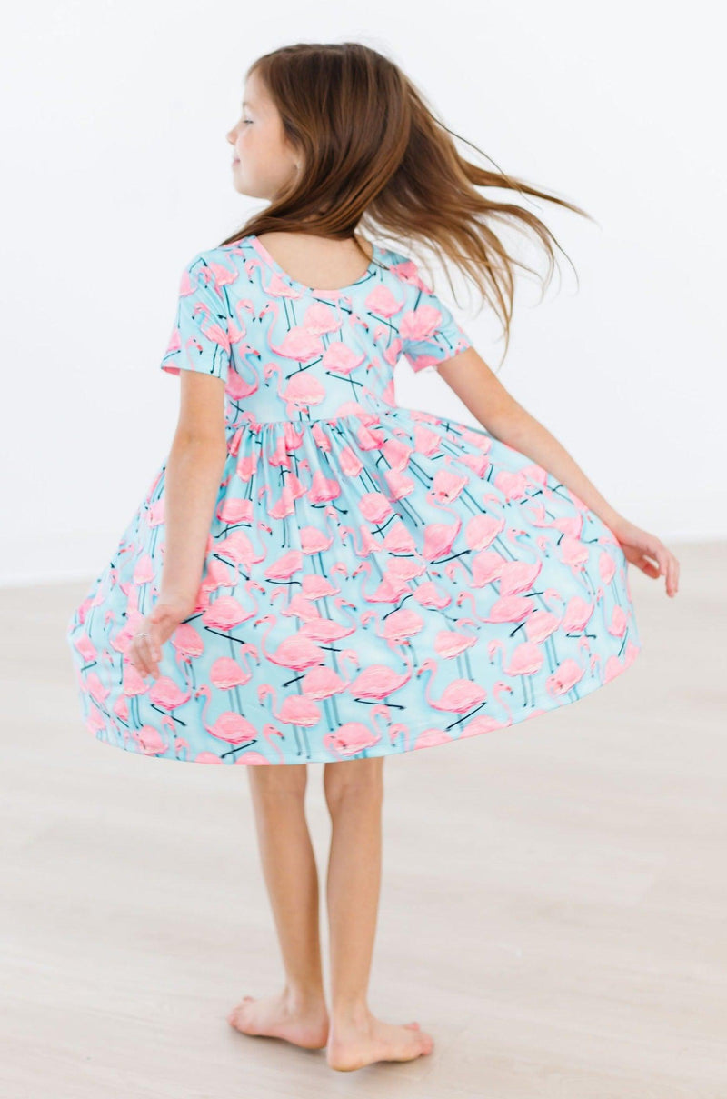 A girl spins elegantly in the Pretty in Pink Flamingos S/S Pocket Twirl Dress, highlighting the flowing design and colorful flamingo print.