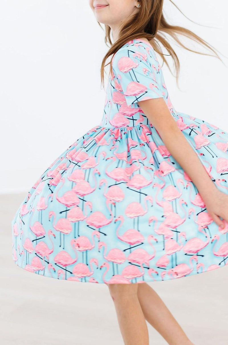 A joyful child spinning in the Pretty in Pink Flamingos S/S Pocket Twirl Dress, featuring a playful pink flamingo print, perfect for twirling adventures.