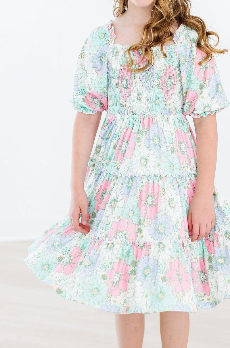 Close-up of a girl in the Minty Meadow Smocked Ruffle Dress, highlighting the beautiful floral design and flowing ruffle tiers.