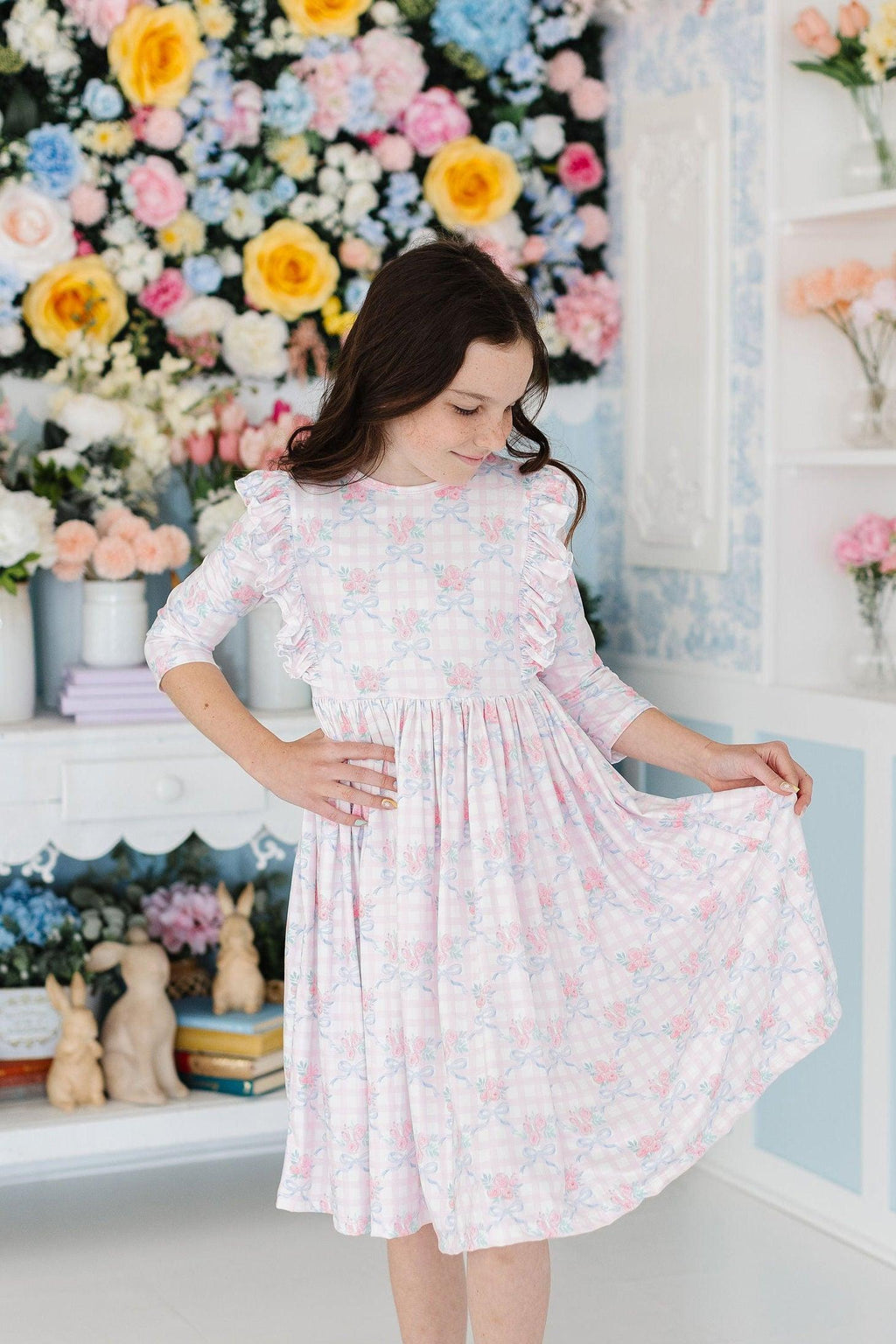 Little girl wearing the Ribbons & Roses 3/4 Sleeve Ruffle Twirl Dress, twirling happily in front of a decorative floral backdrop.