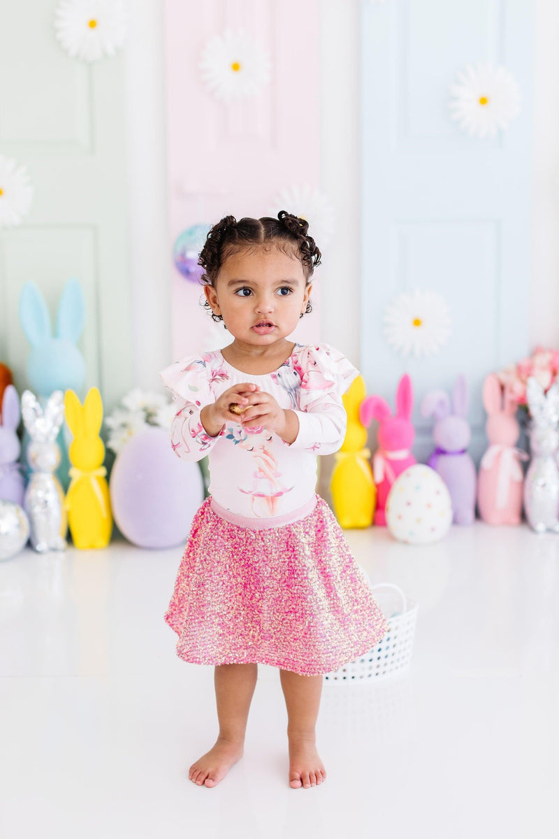 Adorable toddler showcasing her Hot Pink Sequin Twirl Skort from Mila & Rose, standing confidently against a colorful pastel backdrop of playful bunnies and spring decorations.