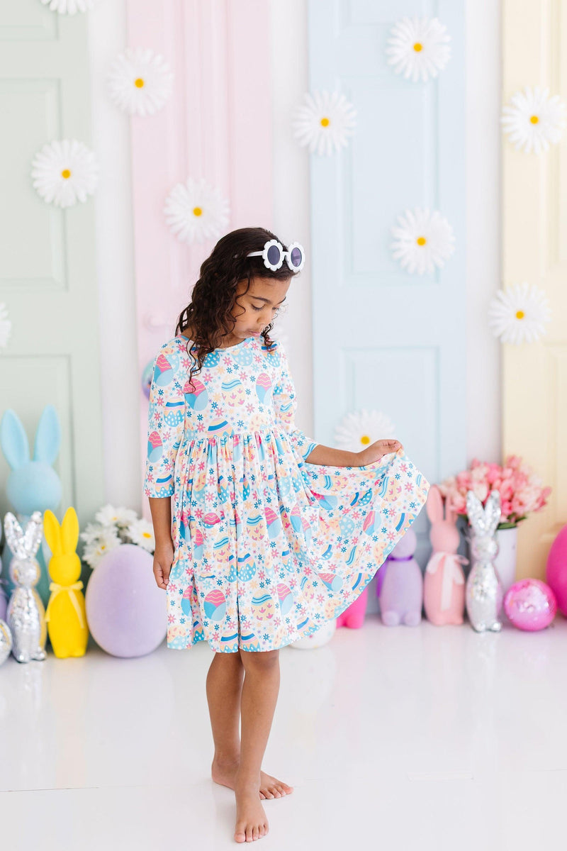 A girl gracefully twirls in her Egg-cellent 3/4 Sleeve Pocket Twirl Dress, with vibrant decorations around her, capturing the essence of joy and playfulness.