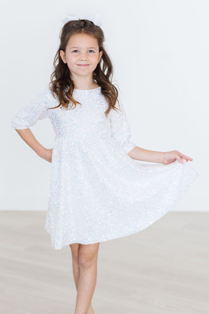 A girl standing confidently in a SALE White Sparkly Disco Sequin Party Dress for Girls, smiling and showcasing the dress's sparkly details.