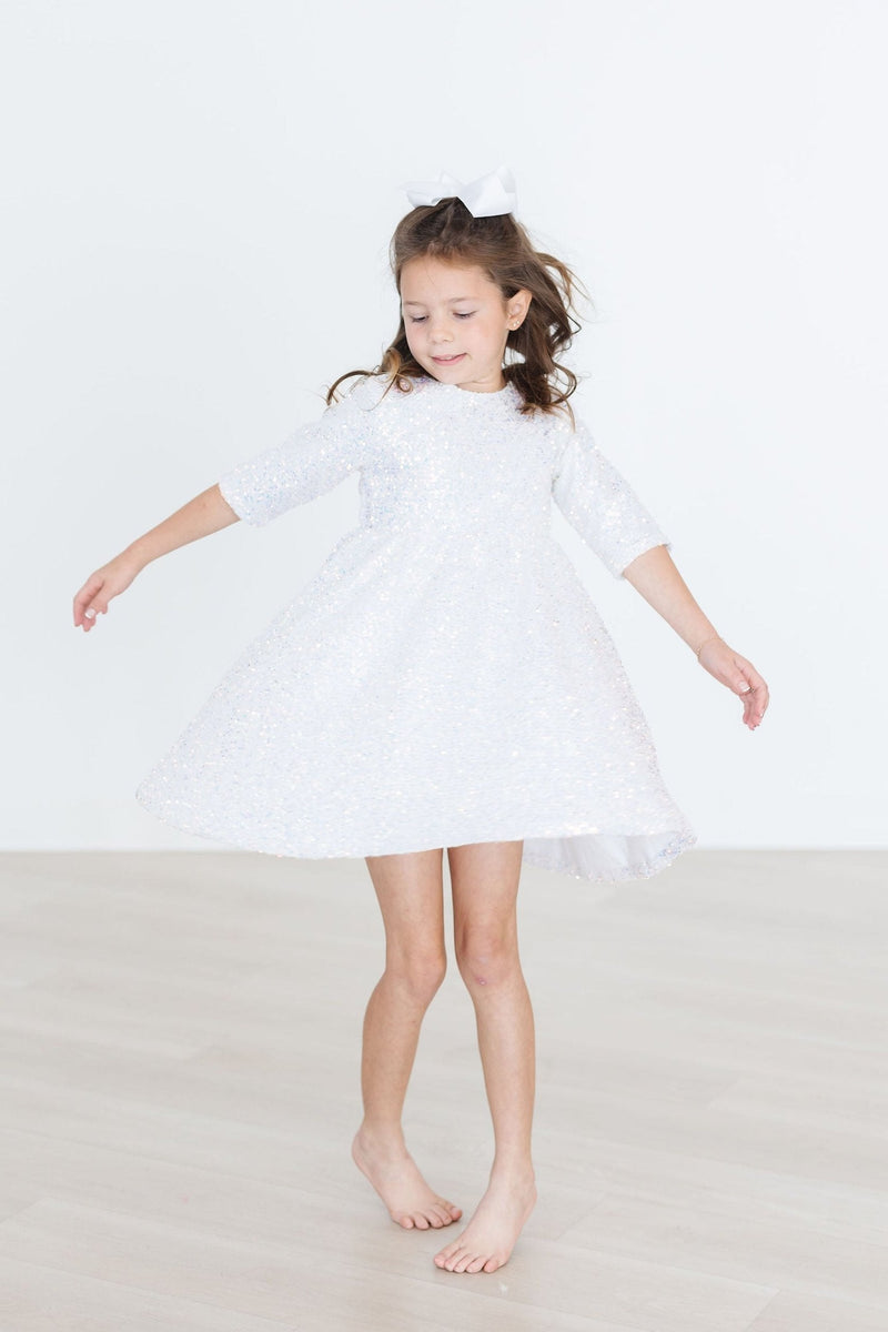 A girl in a charming white sequin party dress, twirling gracefully as she enjoys the moment, showcasing the dress's beauty.