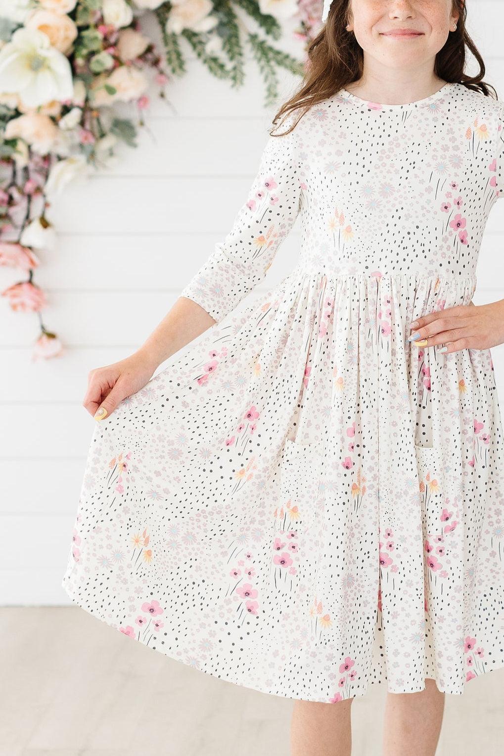 Whimsical Wildflowers 3/4 Sleeve Pocket Twirl Dress modeled by a young girl, showcasing the vibrant floral print and twirl-friendly full skirt.